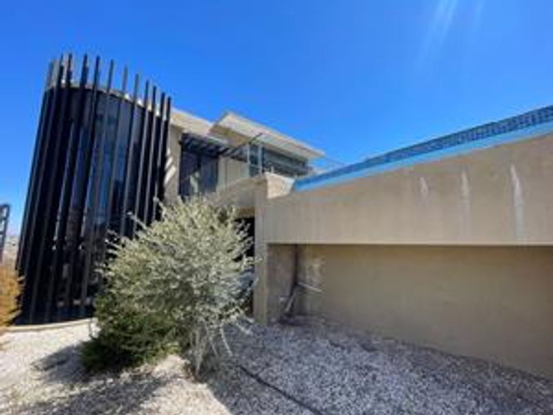Rear elevation of a modern home featuring a swimming pool, vertical architectural fins, and a balcony, showing some exterior wall staining.