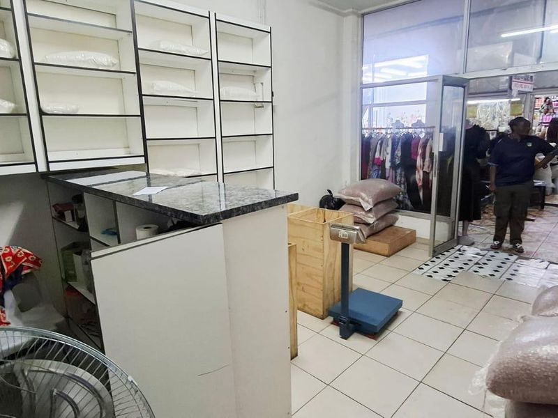 A functional retail utility or storage space featuring built-in shelving units, a service counter, and tiled flooring with direct access to the storefront.