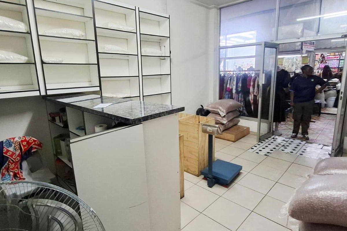 A functional retail utility or storage space featuring built-in shelving units, a service counter, and tiled flooring with direct access to the storefront.