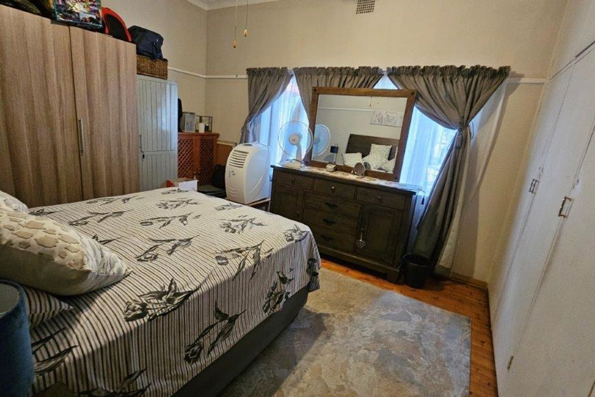 A bedroom featuring built-in wardrobes, timber flooring, and large windows with curtain treatments.