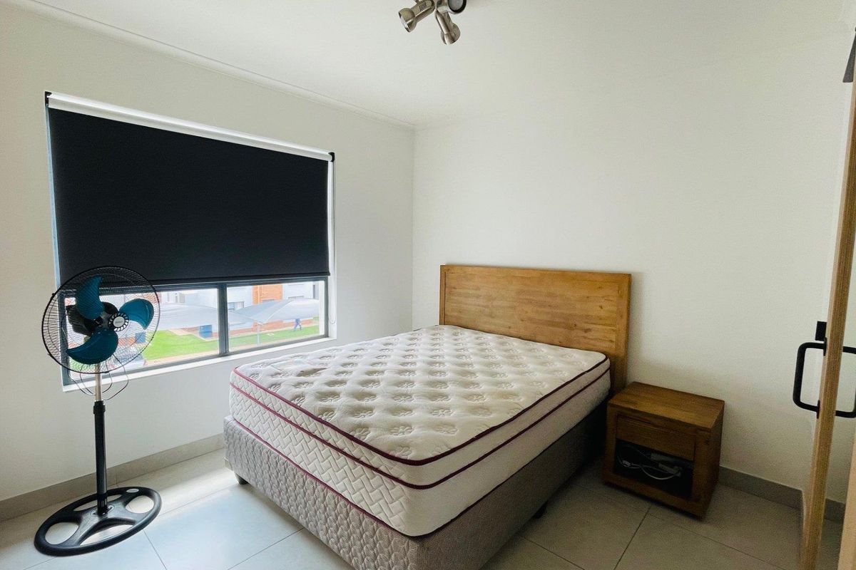 A bright bedroom featuring tiled flooring, a large window with a fitted roller blind, and built-in cupboard space.
