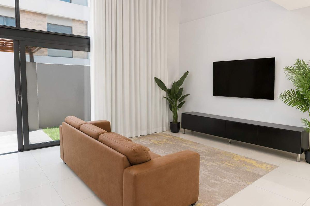 A bright, modern living room featuring double-volume ceilings, large floor-to-ceiling windows, and direct access to a private outdoor area.
