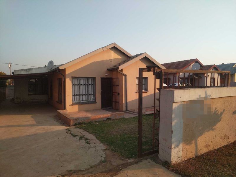 Front view of a single-story house featuring a concrete driveway, carport, and perimeter boundary wall with a security gate.