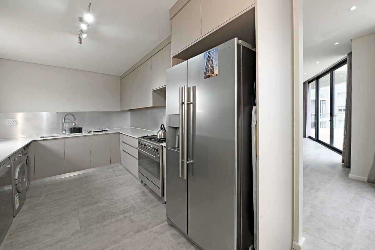 Modern kitchen featuring sleek cabinetry, stainless steel gas range, integrated sink, and tiled flooring, seamlessly flowing into the adjacent living area.