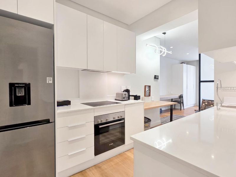 Modern open-plan kitchen featuring sleek white cabinetry, quartz countertops, integrated appliances, and high-quality finishes, seamlessly flowing into the adjacent living and dining area.