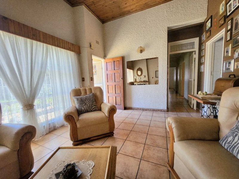 A living room featuring tiled flooring, a timber ceiling, and textured walls, providing a dated but functional space with direct access to the hallway.