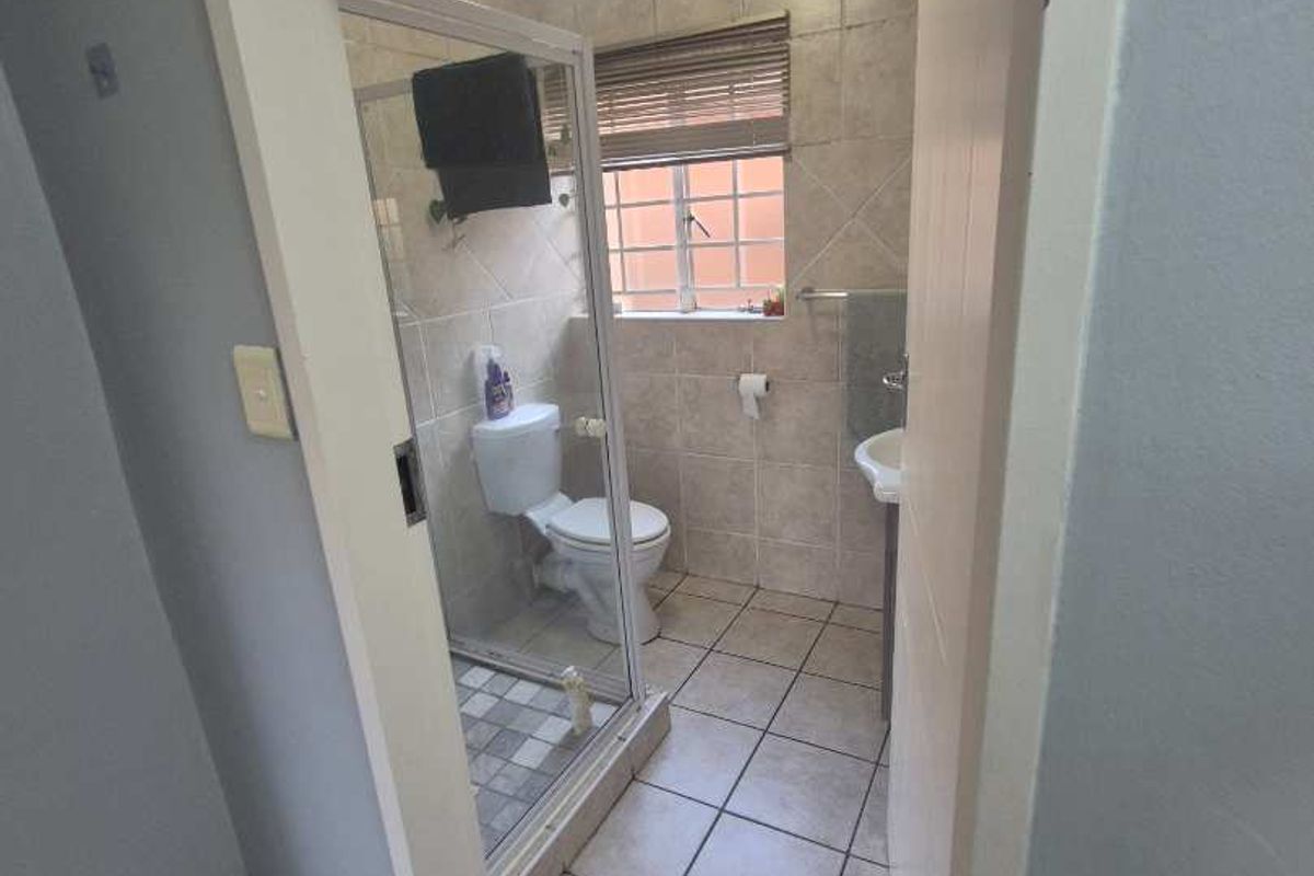A functional bathroom featuring a glass-enclosed shower, tiled walls and flooring, and a window for natural light.