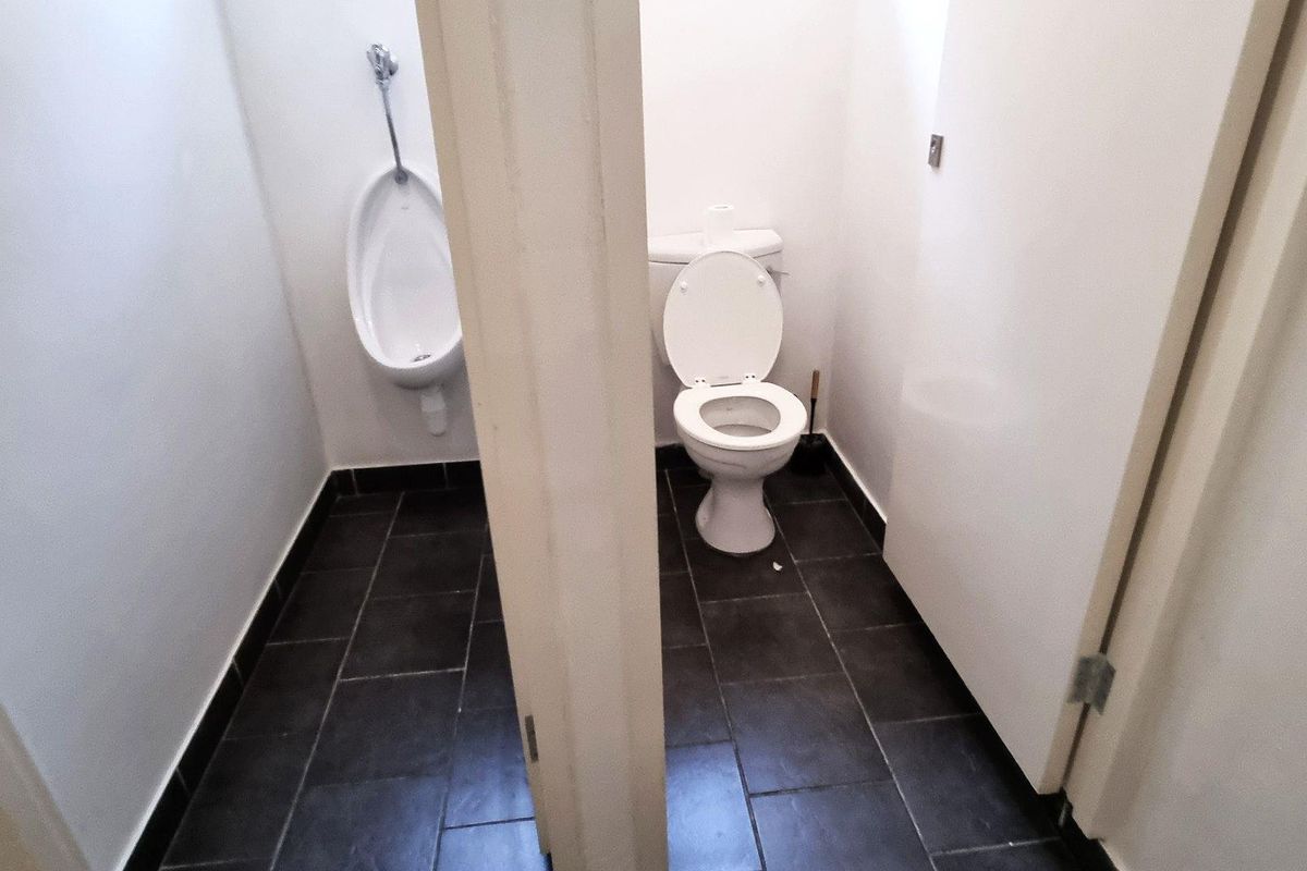 A functional restroom facility featuring a wall-mounted urinal and a standard flush toilet with dark tiled flooring.