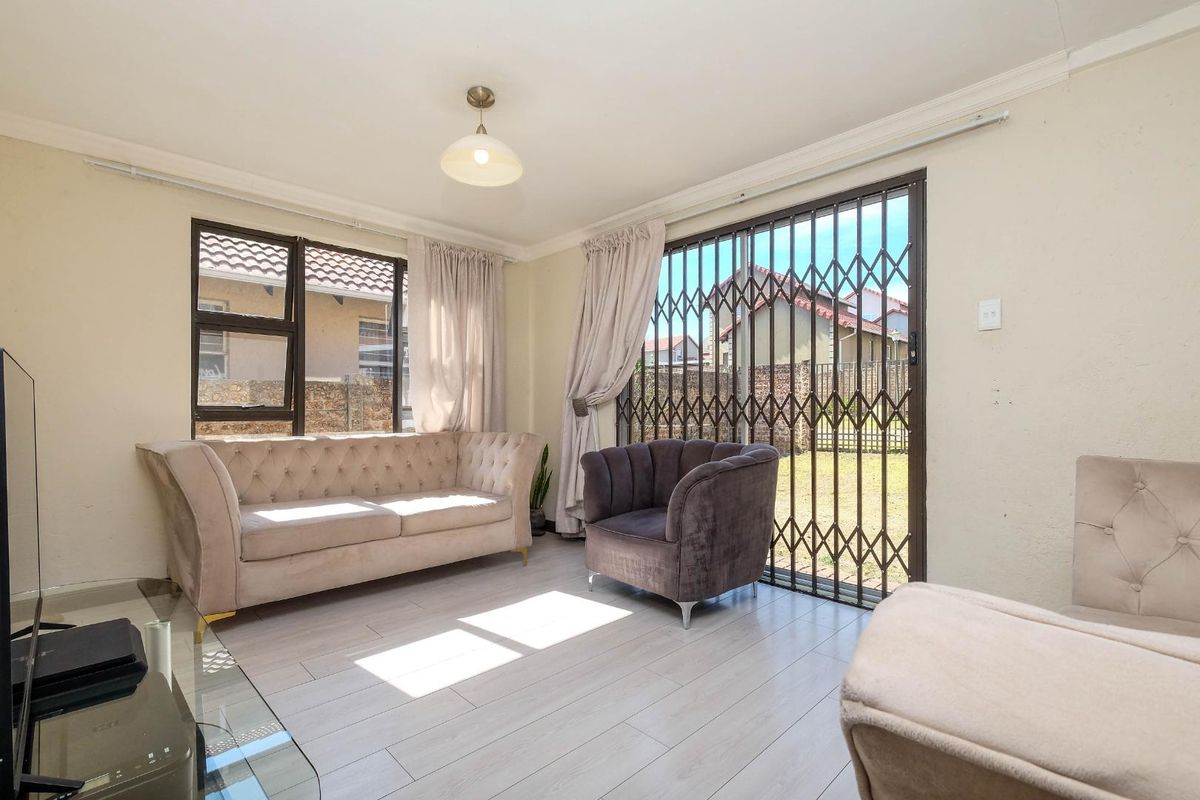 A bright living room featuring light laminate flooring, aluminium window frames, and a sliding glass door with a security gate leading to the garden.