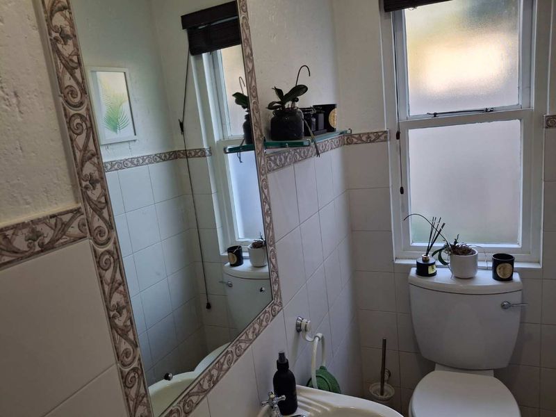 A functional bathroom featuring tiled walls with decorative border, a standard toilet, a washbasin, and a frosted glass window for privacy.