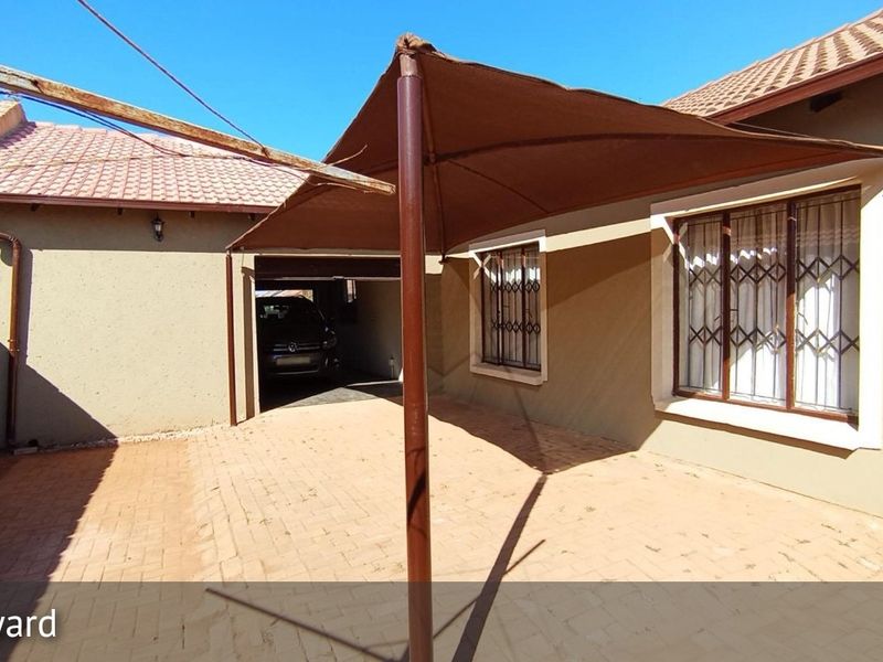 Rear exterior view featuring a paved patio area with a shade sail, security bars on windows, and tiled roof.