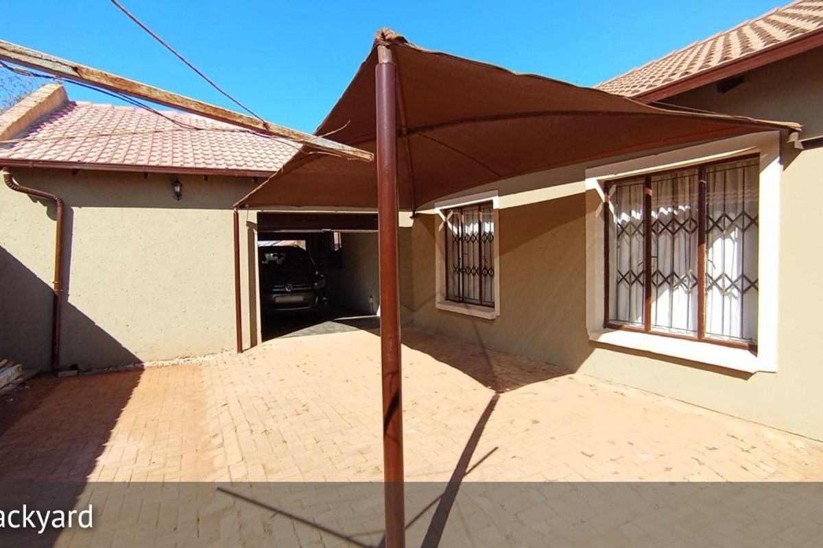 Rear exterior view featuring a paved patio area with a shade sail, security bars on windows, and tiled roof.