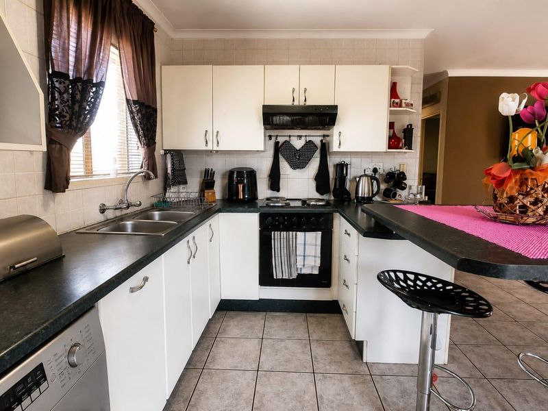 Functional kitchen featuring white cabinetry, dark laminate countertops, a breakfast bar, built-in oven, hob, and tiled flooring with a neutral backsplash.