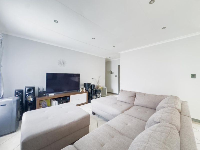 A bright and spacious living room featuring neutral tiled flooring, recessed downlighting, and a clean, minimalist aesthetic.