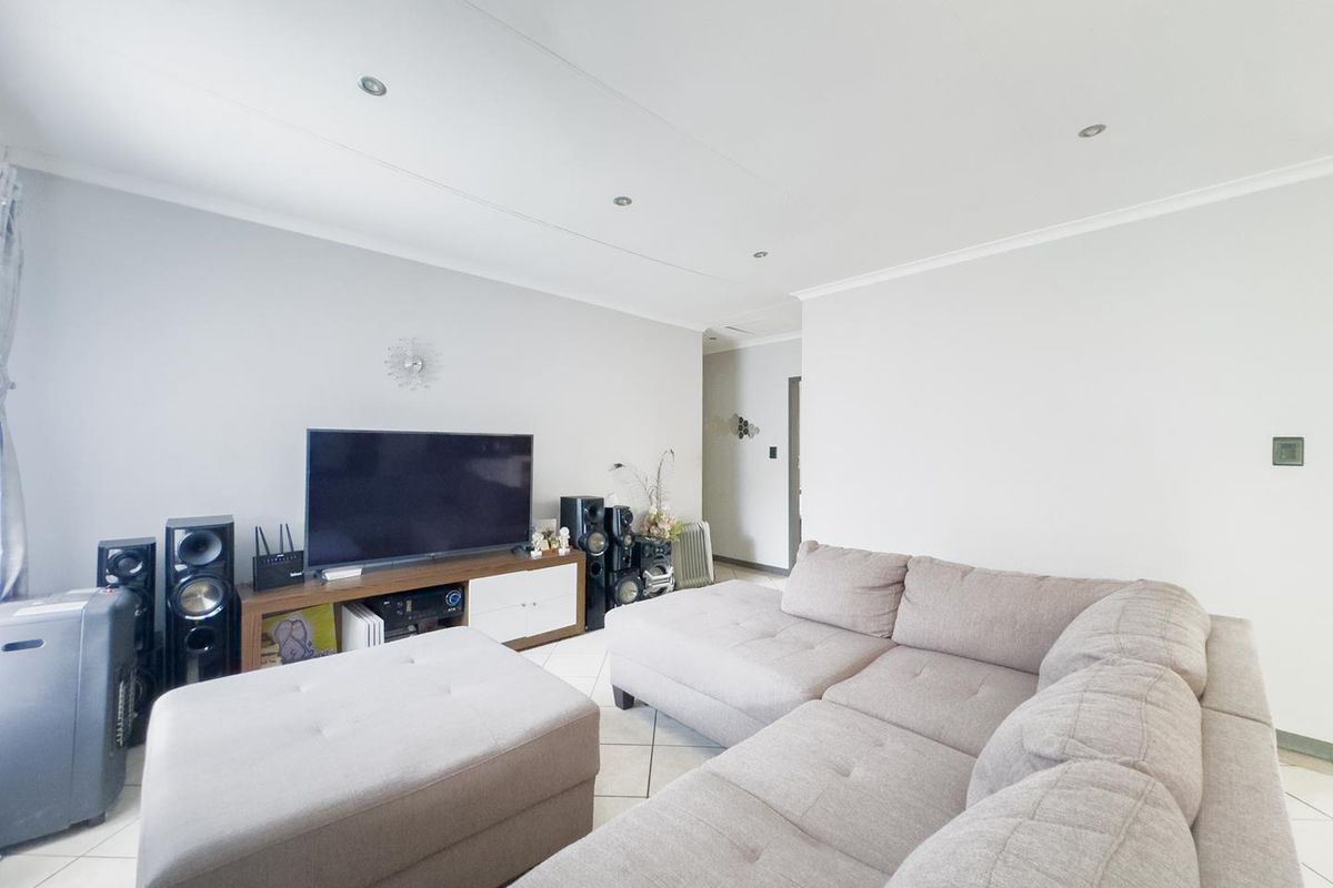 A bright and spacious living room featuring neutral tiled flooring, recessed downlighting, and a clean, minimalist aesthetic.