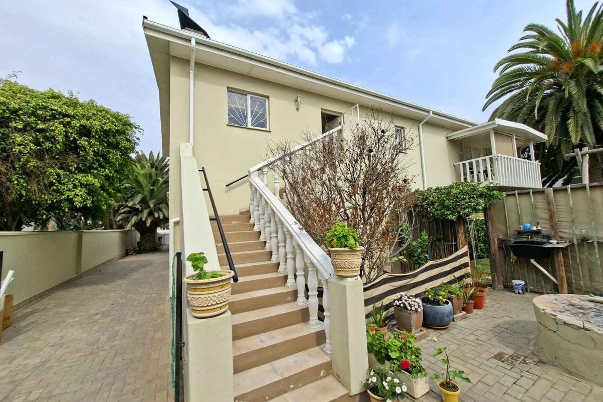 Rear exterior view of the property featuring an external staircase with balustrades, paved courtyard area, and access to the upper level.