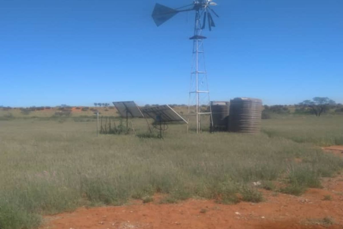 A rural farm landscape featuring a functional windmill, solar panel array, and water storage tanks for agricultural utility.