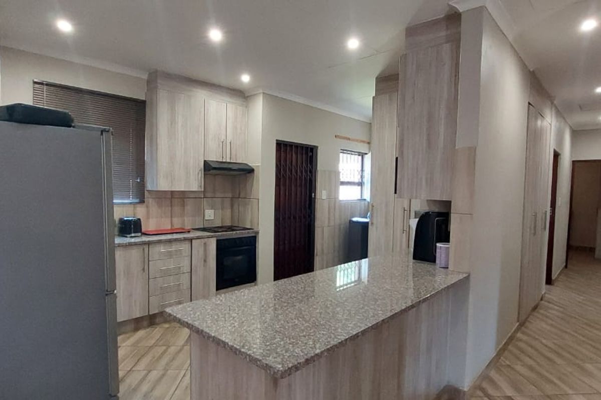 Modern kitchen featuring light wood-grain cabinetry, granite countertops, a breakfast bar, and integrated oven with extractor fan, leading into a tiled hallway.