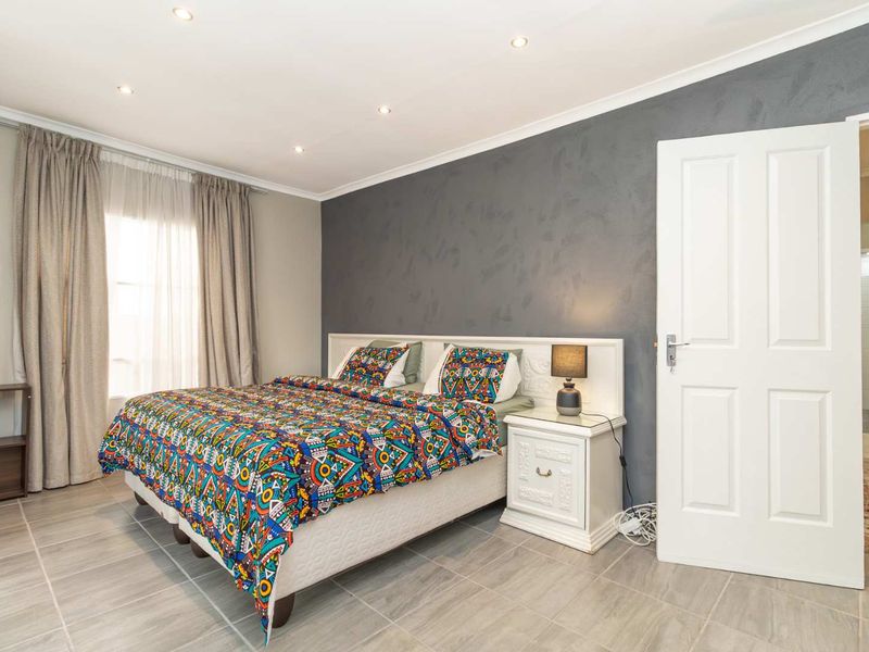 A well-maintained bedroom featuring neutral tiled flooring, recessed downlighting, and a feature wall, with direct access to an adjoining bathroom.