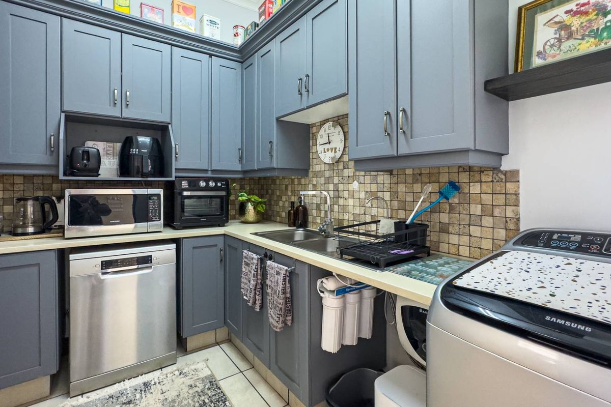 A functional kitchen featuring grey cabinetry, tiled backsplash, stainless steel sink, and integrated space for a dishwasher and laundry appliances.