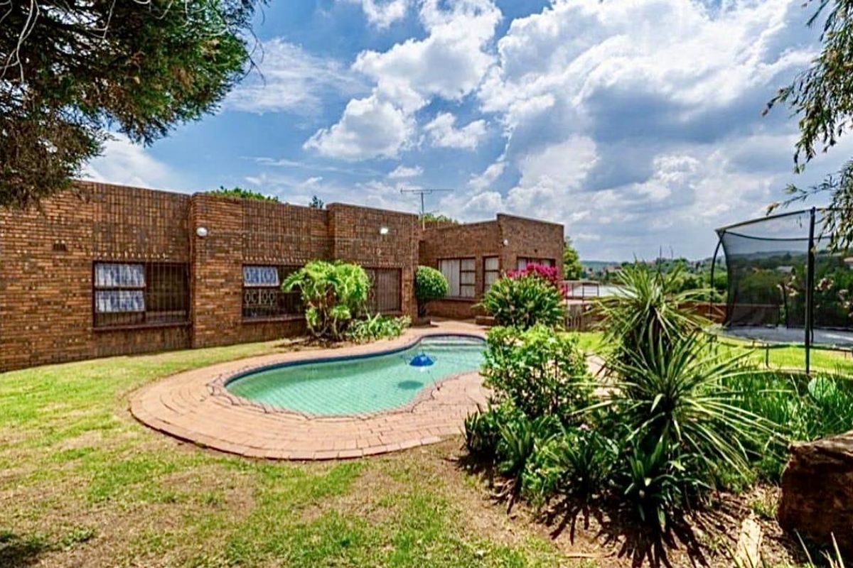 Rear exterior view featuring a face-brick facade, a swimming pool with paved surround, and a landscaped garden area.