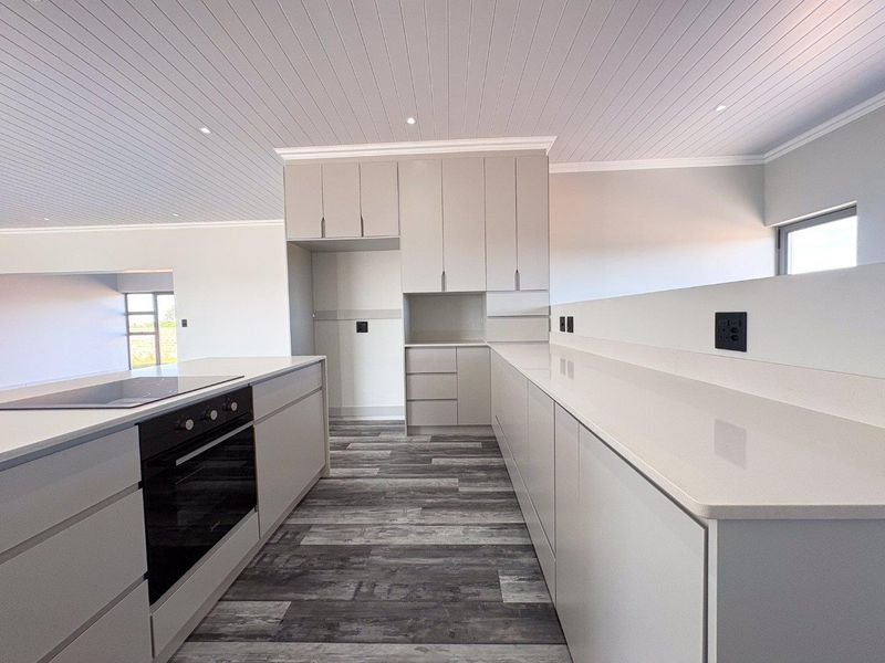 Modern, minimalist kitchen featuring sleek handleless cabinetry, stone countertops, integrated oven and cooktop, and a stylish tongue and groove ceiling.