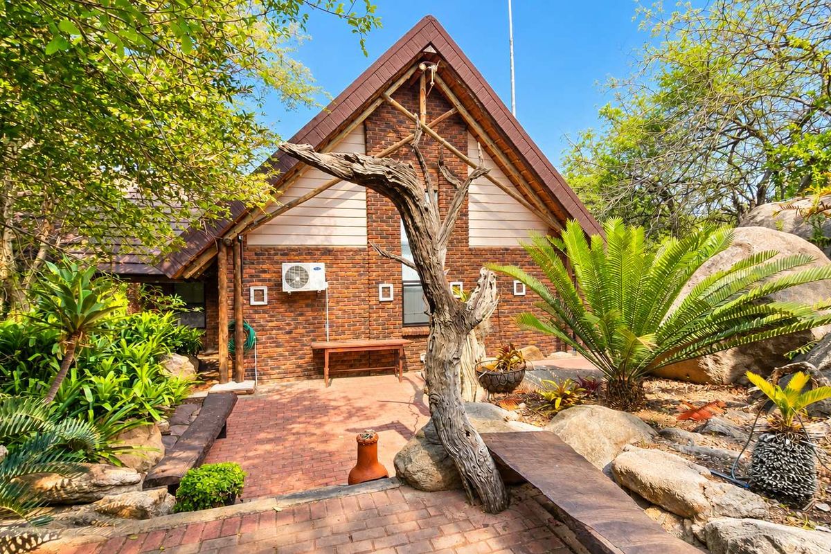 A charming rear exterior view featuring a brick facade, timber accents, and a well-maintained brick-paved patio surrounded by a natural rock garden.