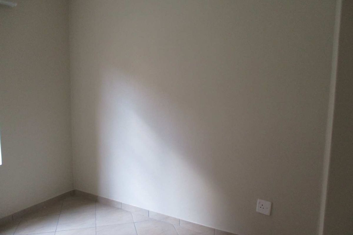 A vacant bedroom featuring neutral painted walls, tiled flooring, and a standard electrical power outlet.