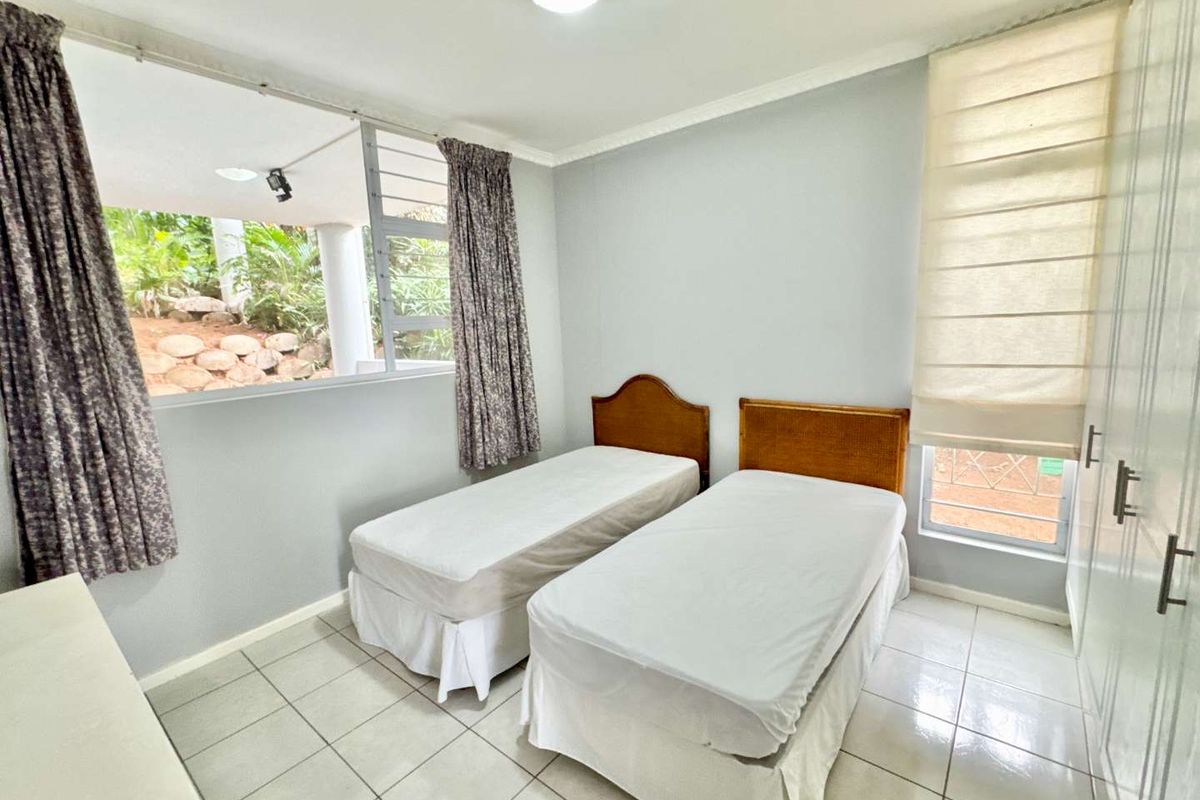 A bright bedroom featuring tiled flooring, built-in cupboards, and large windows providing natural light and views of the surrounding greenery.