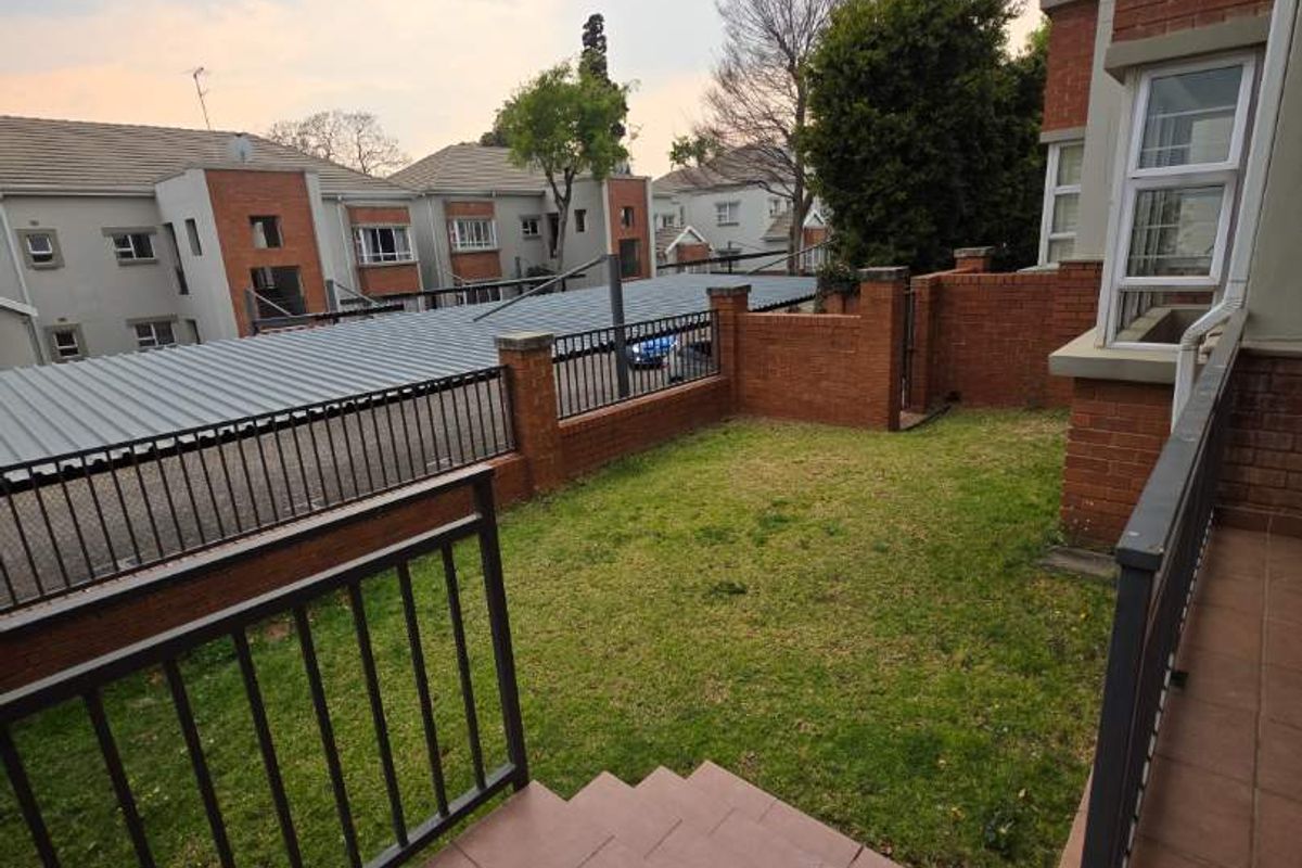 A private rear garden area featuring a tiled patio, metal balustrades, and a small lawn enclosed by brick walls and metal fencing.