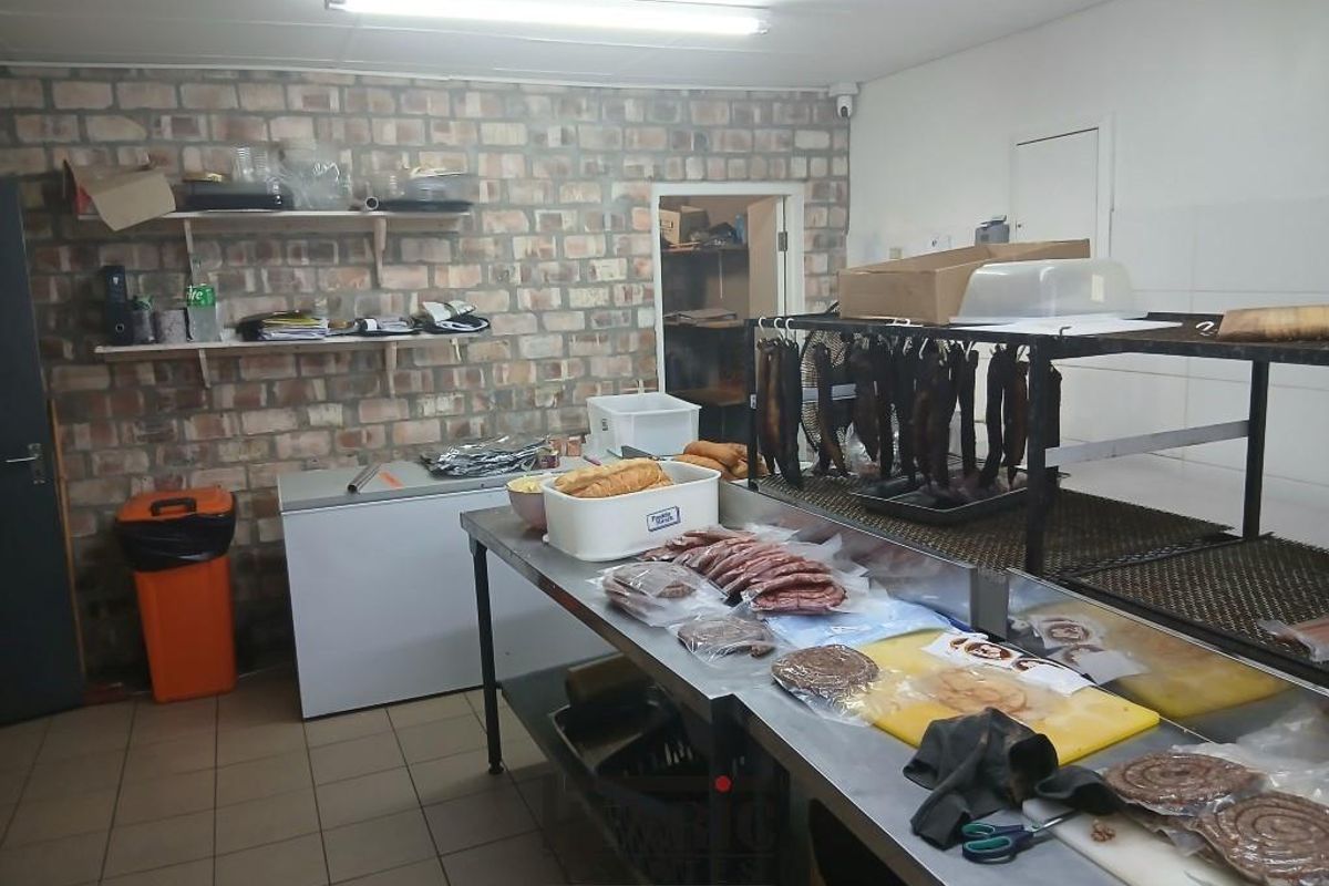 A functional commercial kitchen or food preparation area featuring stainless steel work surfaces, exposed brick walls, and basic utility lighting.