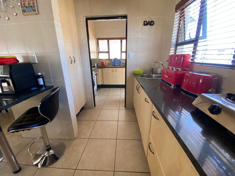 A functional kitchen featuring granite countertops, light wood cabinetry, and tiled finishes, with an adjacent scullery area visible through the doorway.