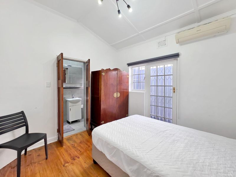 A bedroom featuring timber flooring, a vaulted ceiling, a split-system air conditioner, and direct access to an en-suite bathroom with a security gate.