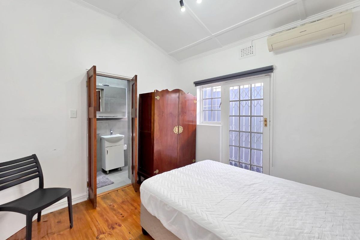 A bedroom featuring timber flooring, a vaulted ceiling, a split-system air conditioner, and direct access to an en-suite bathroom with a security gate.