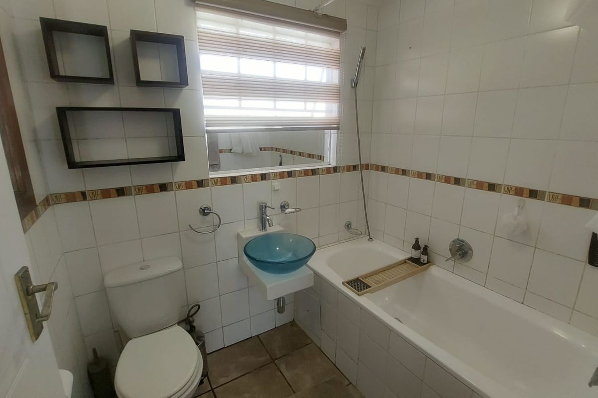 A compact bathroom featuring a white bathtub, wall-mounted glass vessel sink, toilet, and tiled walls with a decorative border.