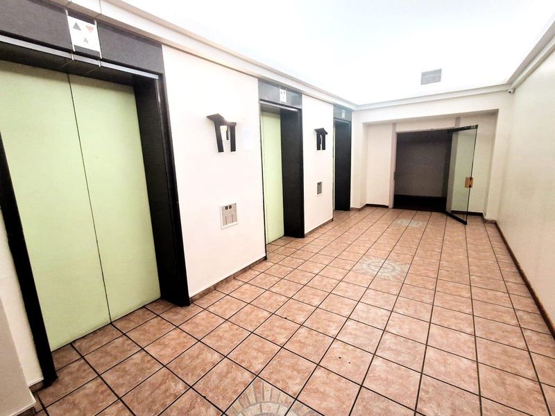 A clean and functional apartment building elevator lobby featuring tiled flooring, multiple elevator access points, and modern wall-mounted lighting.