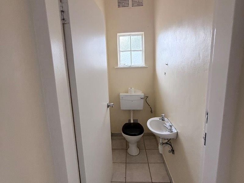 A compact guest bathroom featuring a wall-mounted basin, toilet, and tiled flooring, presenting a functional space in need of cosmetic updates.