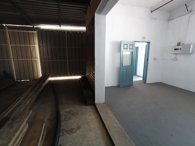 Industrial utility space featuring concrete flooring, exposed fire sprinkler piping, and an electrical distribution board, with access to an adjacent storage area.