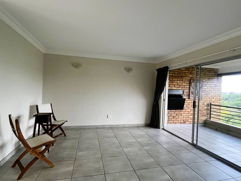 Spacious living area featuring neutral tiled flooring, crown molding, and large sliding glass doors that open onto a private balcony.