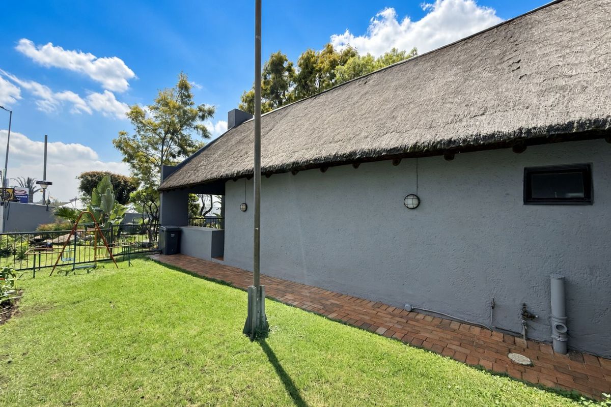 Rear exterior view of the property featuring a thatched roof, brick paved walkway, and a landscaped garden area.
