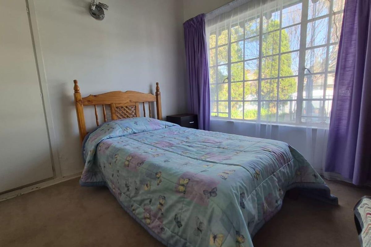 A bedroom featuring a large grid-pattern window that allows natural light, complemented by a wall-mounted light fixture and carpeted flooring.