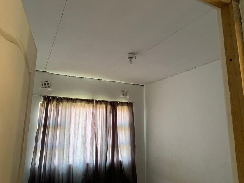 An empty bedroom featuring a window with curtains, ceiling vents, and visible signs of wear including ceiling cracks and joint separation.