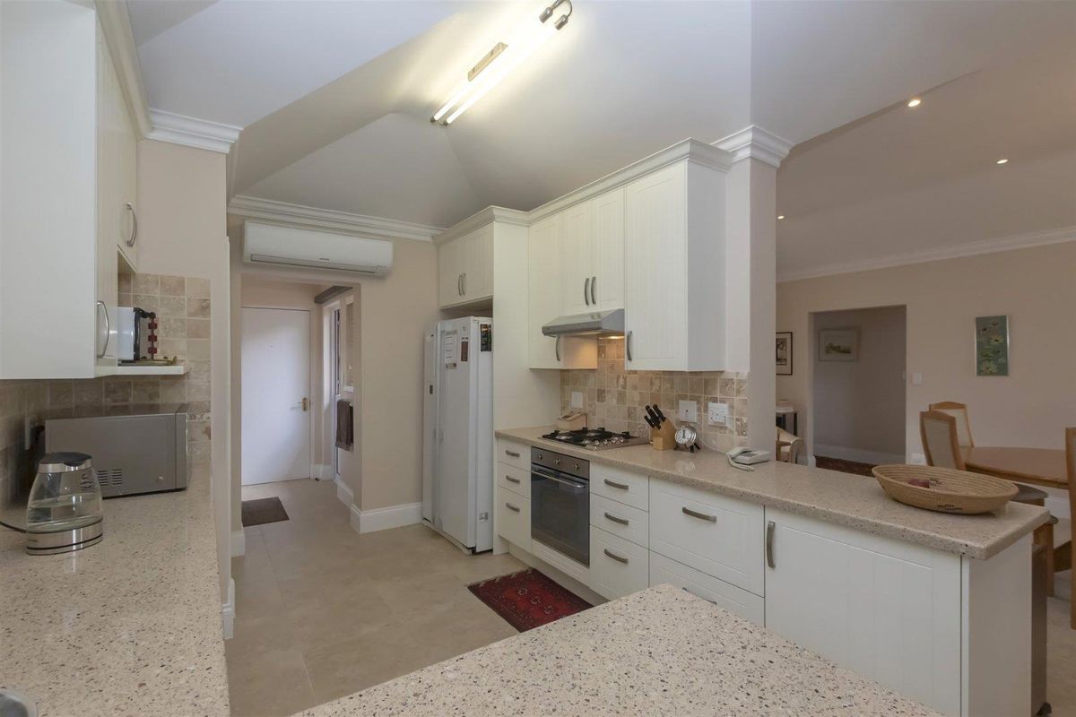 A well-maintained kitchen featuring stone countertops, built-in cabinetry, a gas hob, oven, extractor fan, and tiled flooring with an open-plan layout.