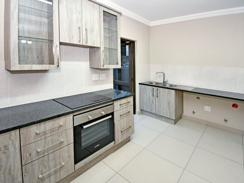 Modern kitchen featuring light wood-grain cabinetry, granite countertops, built-in oven, electric hob, and tiled flooring with ample space for appliances.