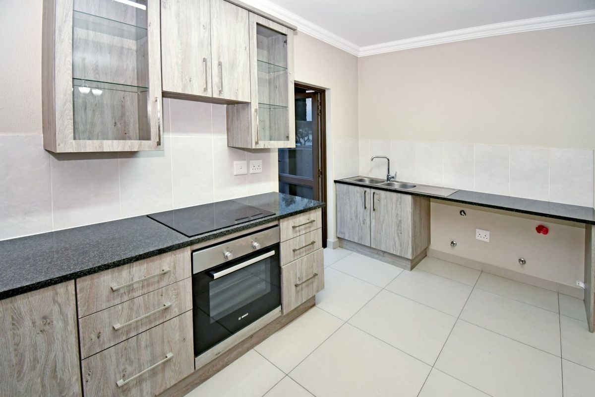 Modern kitchen featuring light wood-grain cabinetry, granite countertops, built-in oven, electric hob, and tiled flooring with ample space for appliances.