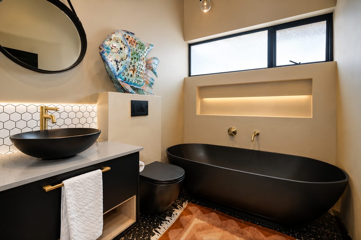 Modern bathroom featuring a matte black freestanding bathtub, vessel sink, gold fixtures, built-in wall niche, and stylish terrazzo flooring.