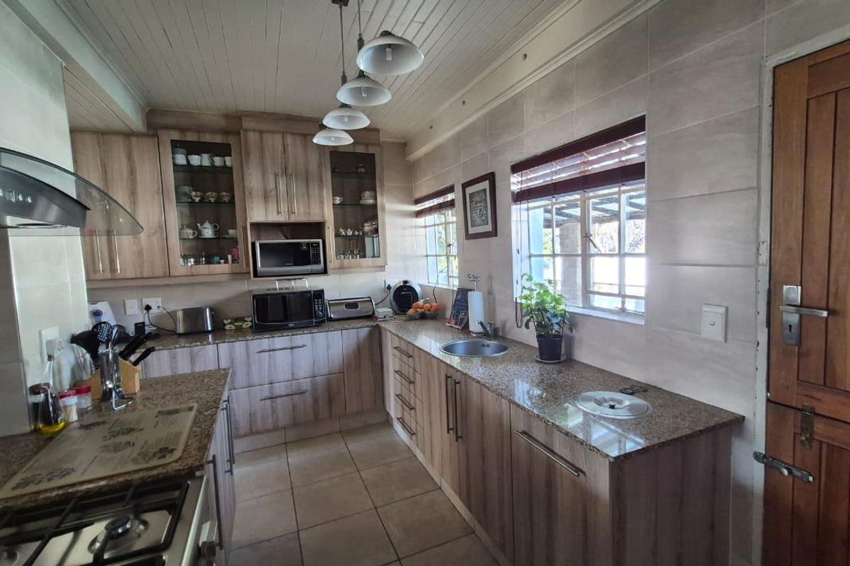 A well-maintained kitchen featuring granite countertops, ample built-in cabinetry, a gas hob with extractor fan, and tiled flooring with a timber panelled ceiling.