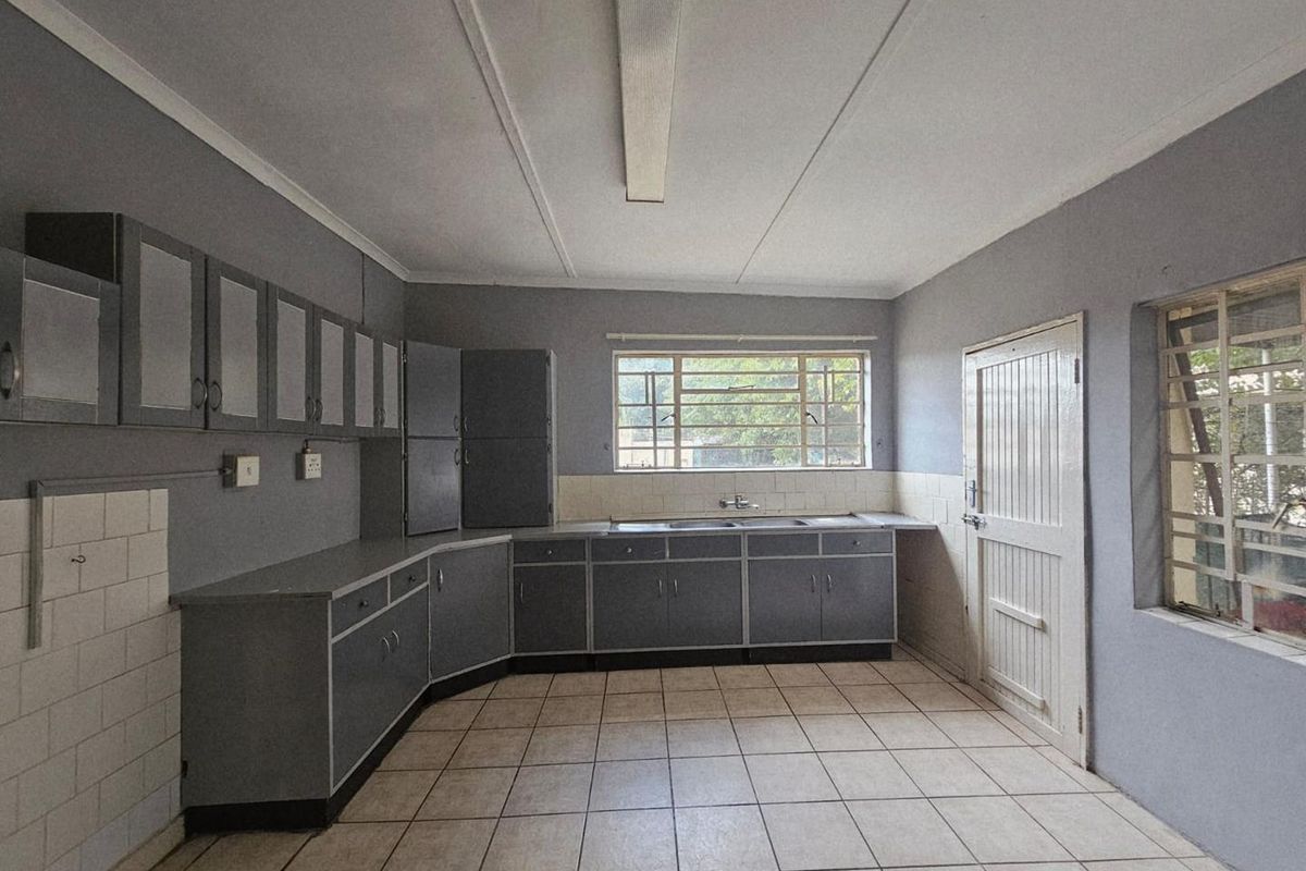 A functional kitchen space featuring grey cabinetry, tiled flooring, and a double sink, offering a blank canvas for potential renovation and modernization.