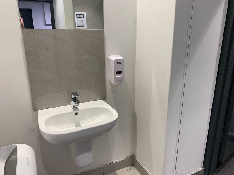 A clean, functional commercial bathroom featuring a wall-mounted basin, chrome mixer tap, and wall-mounted soap dispenser.