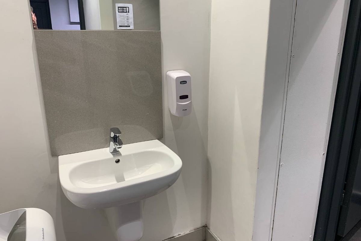 A clean, functional commercial bathroom featuring a wall-mounted basin, chrome mixer tap, and wall-mounted soap dispenser.